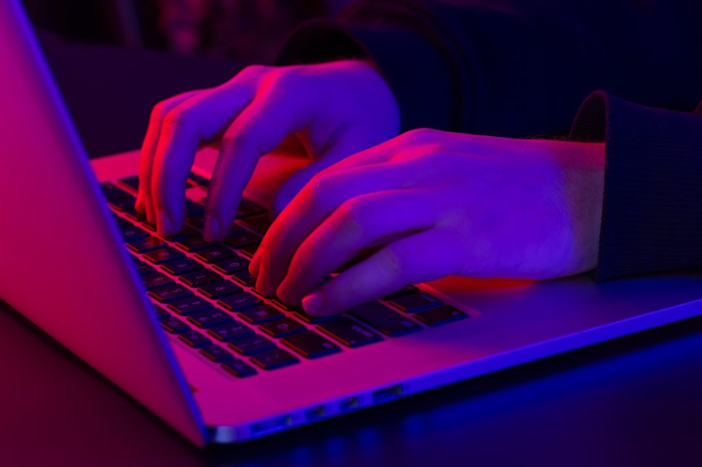 A man uses a laptop, close-up, male hands in neon lighting.